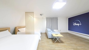 A hotel room with a bed, a sofa, a small table, and a wall-mounted Disney+ screen.