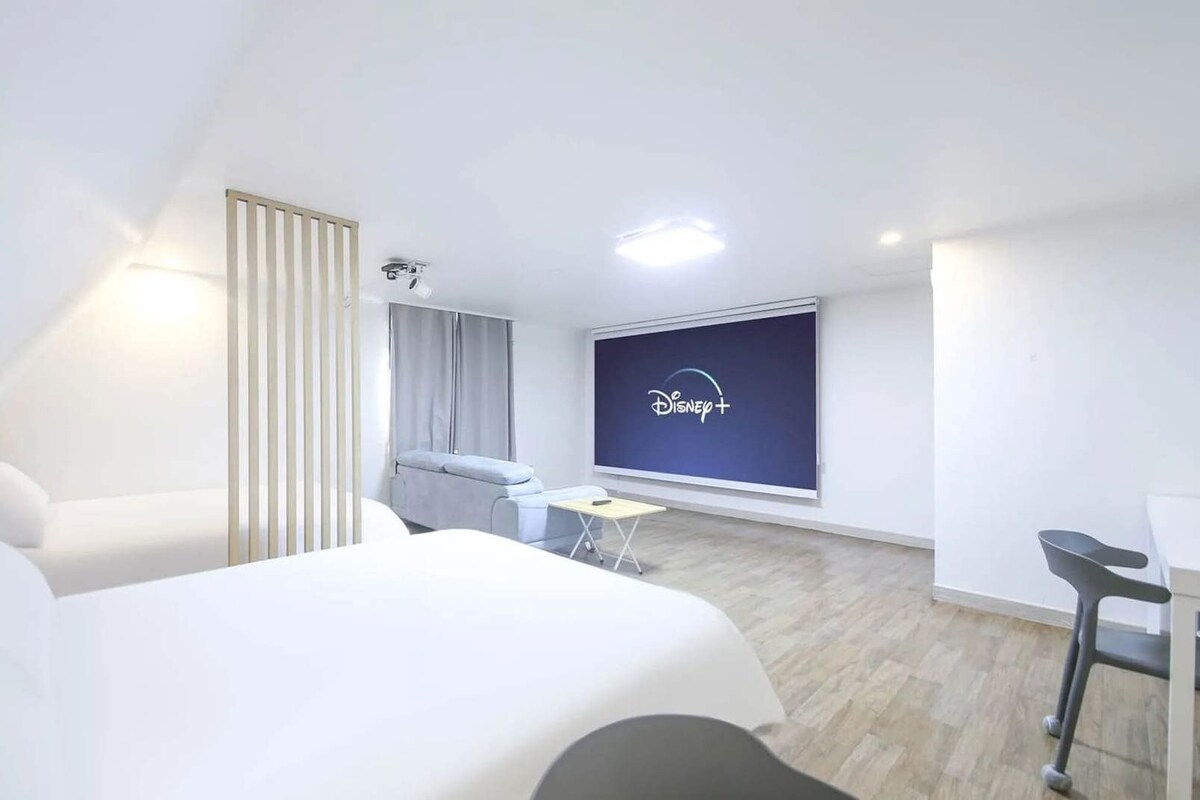 Ein Hotelzimmer mit Bett, Schreibtisch, Stuhl, einem Fernseher, der Disney+ anzeigt, und einem Fenster mit Vorhängen.