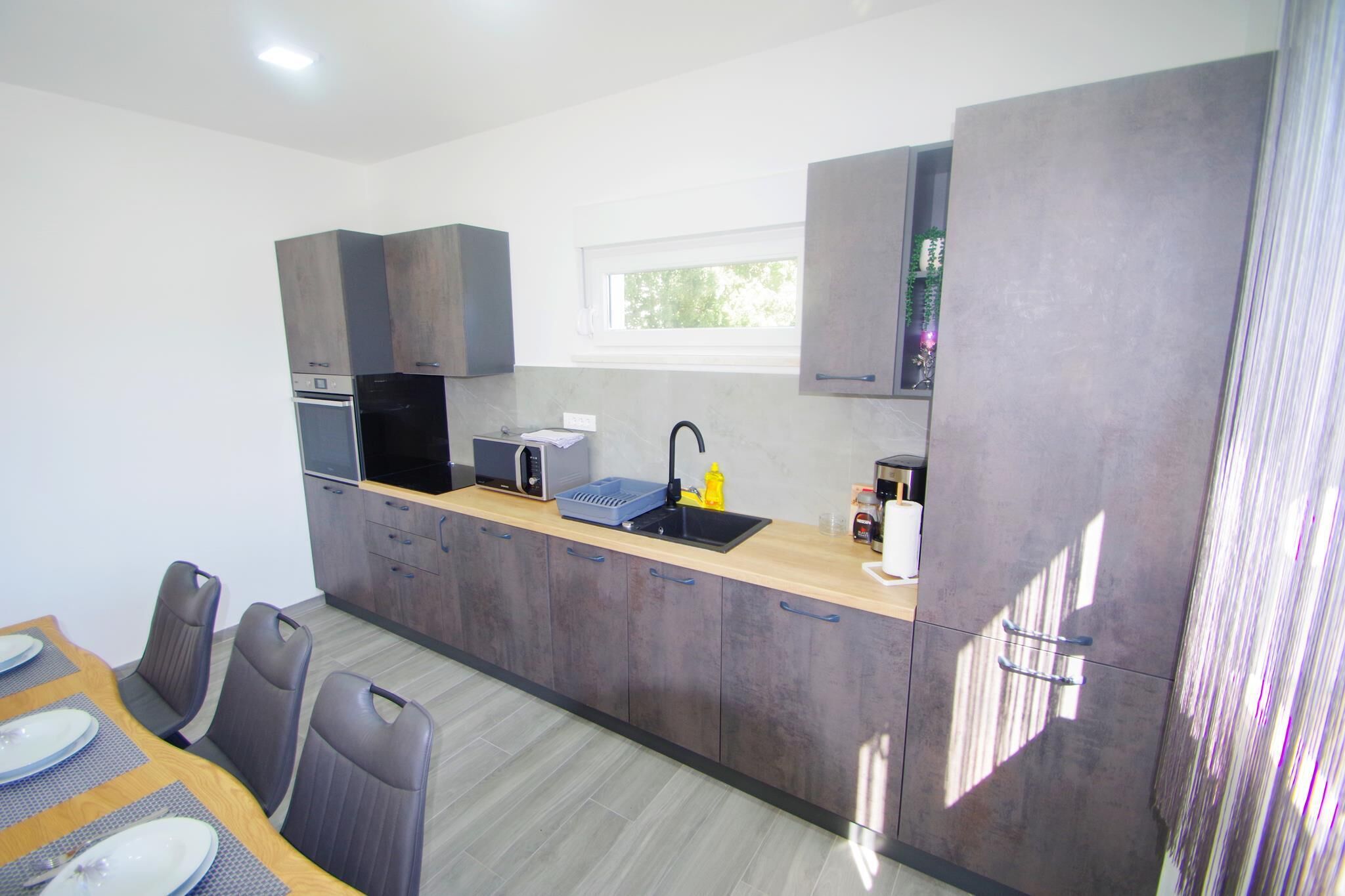 A modern kitchen with dark cabinets, a wooden countertop, and a window above the sink.
