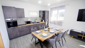 Une cuisine moderne dotée d’appareils électroménagers intégrés, un coin repas avec une table et des chaises en bois, et un téléviseur fixé au mur.