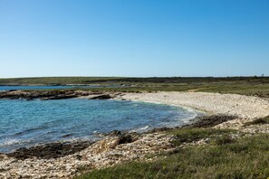 A coastal landscape with a rocky shoreline, clear blue water, and grassy hills in the background. - Brand new villa with private pool on peaceful location (Šišan)