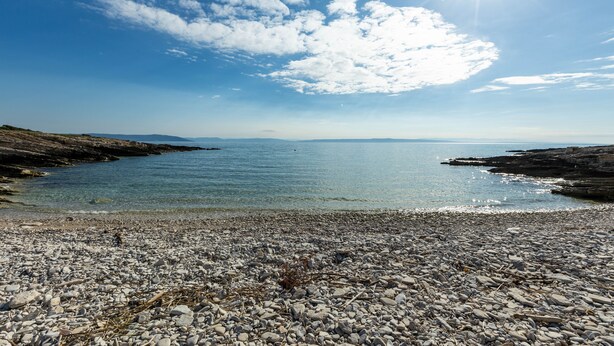 Une plage rocheuse, avec une eau claire et une côte visible au loin.