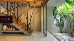 Un intérieur moderne avec un escalier, un téléviseur diffusant du contenu de « NETFLIX », et un petit jardin intérieur.