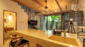 Une cuisine moderne dotée d’un grand îlot central, de chaises en bois, d’un ventilateur de plafond et offrant une vue sur la verdure environnante.