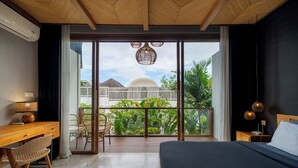 Une chambre avec un grand lit, un bureau en bois, une chaise et un balcon offrant une vue sur la verdure et les bâtiments.