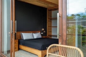 Un dormitorio con cama de madera, cabecera negra y puerta de vidrio que da a un balcón con plantas.