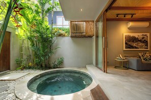 Un área de piscina interior moderna con un jacuzzi, rodeada de exuberante vegetación y una zona de estar con sofá y mesita auxiliar.