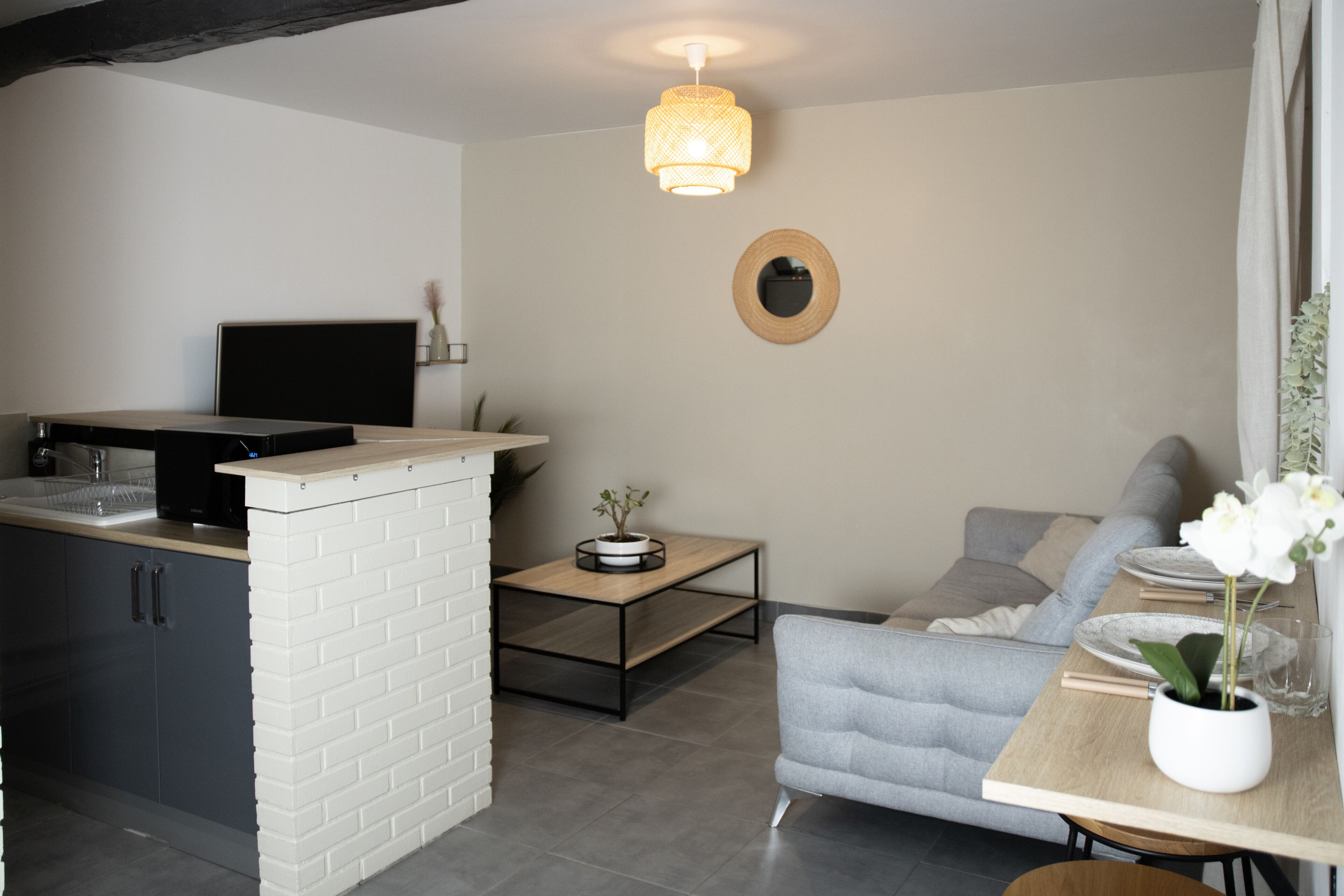 A modern kitchen with a built-in stove, a dining area with a table and chairs, a sofa, and a hanging light fixture.