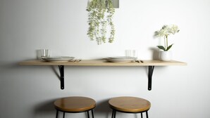 Et minimalistisk spiseområde med et træbord, to barstole, en hængende plante og en orkidé i potte.
