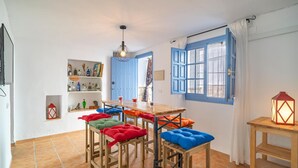 Una habitación con una mesa de madera, cojines coloridos, una puerta azul y un farol en una mesita.