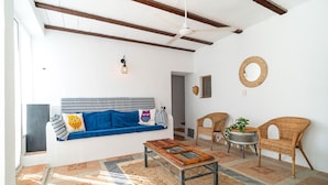 Una sala de estar con un sofá azul, sillas de mimbre, una mesa de centro de madera y un tapete estampado.