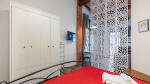 Une chambre avec une couvre-lit rouge, une serviette blanche, un téléviseur fixé au mur et une armoire blanche.