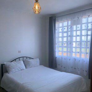 Relax in a cozy space with a single bed, geometric-patterned light fixture, and a window with a subtle patterned curtain.