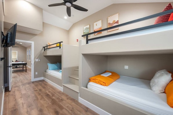 A room with bunk beds, a ceiling fan, and a TV mounted on the wall.