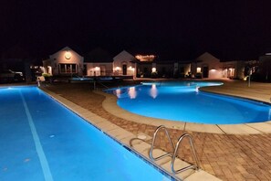 A nighttime swimming pool area with a clear water surface, surrounded by buildings with illuminated signs. - Gaming, Pool, Relaxing, and Memories are all made at After Dune Delight! (Hurricane)