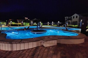 Ein Poolbereich bei Nacht mit Whirlpool, Liegestühlen und einem Pflasterweg.