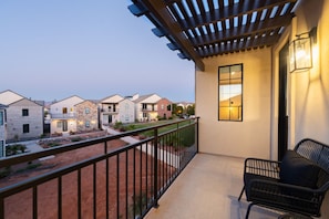 A balcony with a pergola, a view of neighboring houses, and a small seating area with a chair and a table.