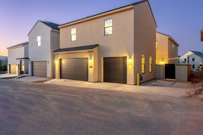 A modern two-story residential building with a garage, a driveway, and a well-lit entrance.