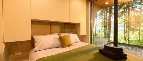 A bedroom with a large bed, a green blanket, and a stack of towels.