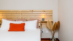 Ein ordentlich bezogenes Bett mit weißen und orangefarbenen Kissen, ein Holz-Kopfteil und ein Nachttisch mit Lampe und Dekoration.