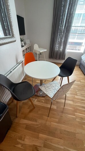 En moderne stue med et rundt hvidt bord, sorte og orange stole, en sort sofa og et stort vindue med gardiner.