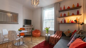 Ein modernes Wohnzimmer mit einer Couch, einem Esstisch mit Stühlen, einem Fernseher und einem roten Teppich.