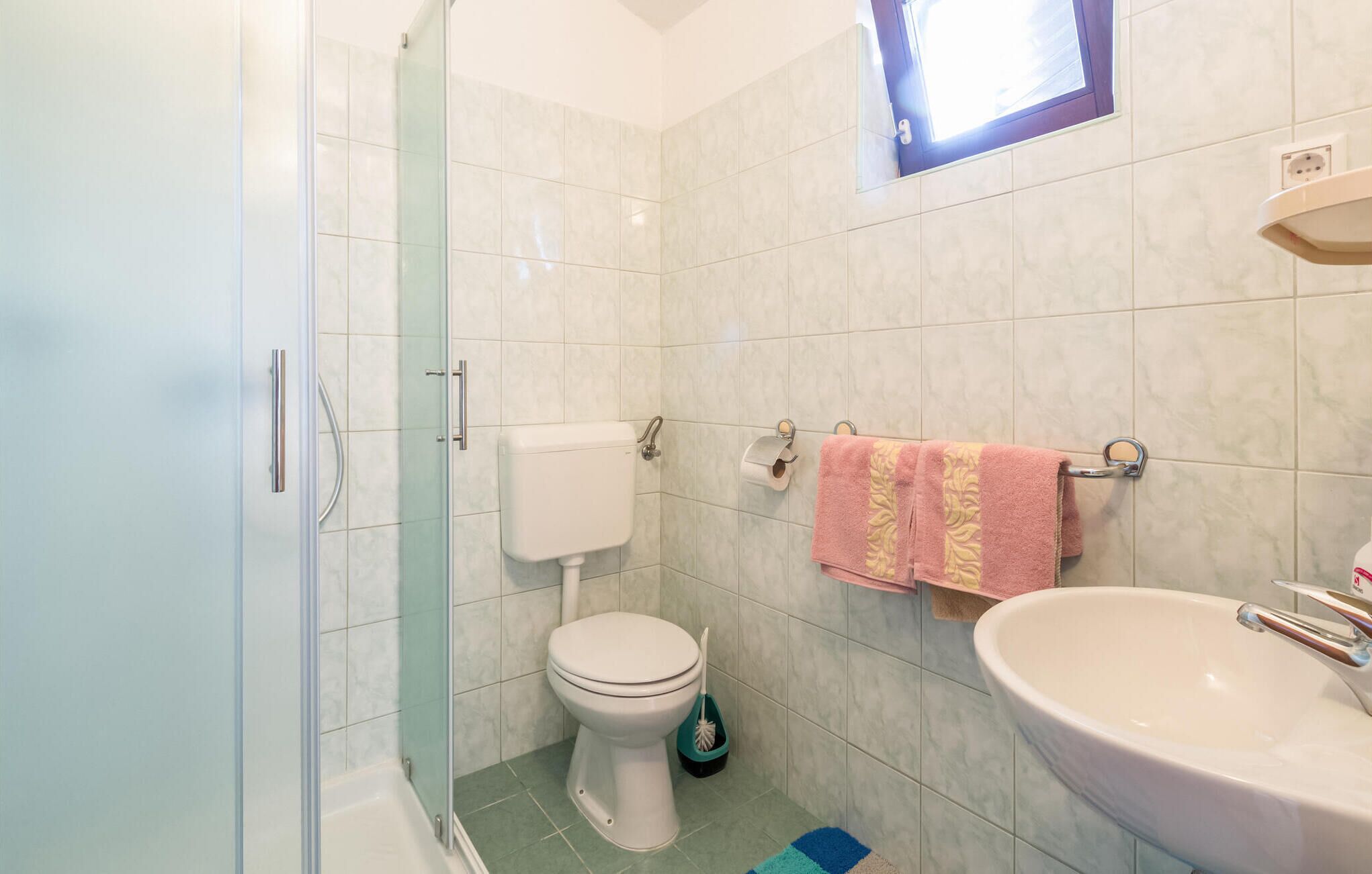 A bathroom with a glass shower enclosure, a toilet, a sink, and a towel rack with towels.