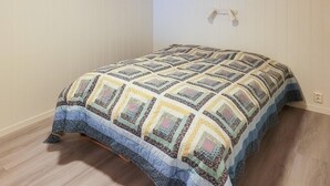 Un petit lit bien fait, avec une couvre-lit à motifs, dans une pièce au plancher de bois et aux murs blancs.