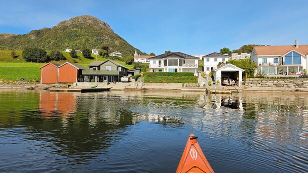 Un quartier résidentiel au bord d’un lac, avec des maisons, un quai et une montagne en arrière-plan.