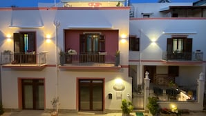 A multi-story building with balconies, a central entrance, and a small garden area. - B&B Le Onde del Mare (San Vito Lo Capo)