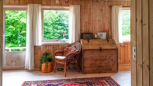 Ein Zimmer mit Holzwänden und -böden, ein Korbstuhl, eine Holzkiste und ein Radio auf einem Fensterbrett.