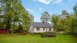 Ein eingeschossiges Haus mit geneigtem Dach, umgeben von einem gepflegten Rasen und dichter Baumvegetation.