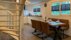 A dining area with a wooden table and chairs, a kitchen in the background, and a staircase leading to an upper level. - 3 bedroom lovely home in Marienberg (Marienberg)