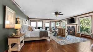 Ein Schlafzimmer mit Bett, Sessel, Kamin und großen Fenstern.
