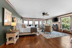 A bedroom with a bed, a chair, a fireplace, and large windows.