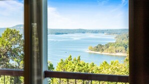 Blick durch ein Fenster auf ein weites Gewässer, umgeben von Bäumen und Hügeln.