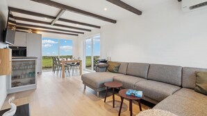 Ein modernes Wohnzimmer mit einer großen Eckcouch, einem Essbereich mit Tisch und Stühlen sowie einer Küchenzeile mit Fernseher und Schränken.