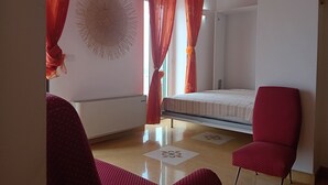 Quarto com beliche, cadeira vermelha, um adorno na parede e janela com cortinas vermelhas.
