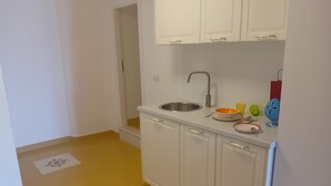 Uma cozinha compacta com armários brancos, pia de aço inoxidável e bancada com uma tigela e uma xícara.