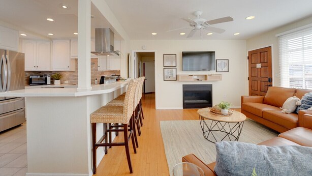 A modern kitchen with white cabinets, a central island, and a dining area with wicker chairs. - Steps to Ocean and Boardwalk, Parking, Outdoor dining! (San Diego)