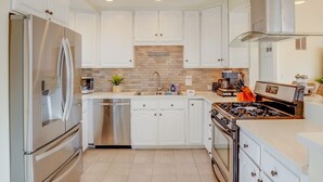 A modern kitchen with white cabinetry, stainless steel appliances, a brick backsplash, and a gas stove. - Steps to Ocean and Boardwalk, Parking, Outdoor dining! (San Diego)