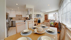 A modern kitchen with white cabinets, a dining area with a wooden table set for four, and a living room with a sofa and a TV. - Steps to Ocean and Boardwalk, Parking, Outdoor dining! (San Diego)