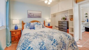 Une chambre comprenant un lit, des tables de chevet, un ventilateur de plafond, une étagère murale décorative et une porte donnant sur une autre pièce.