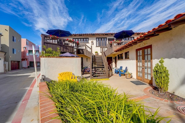 A courtyard with a staircase leading to a balcony, surrounded by buildings with balconies and outdoor seating.