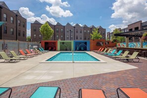 A swimming pool area with lounge chairs and a brick building in the background. - Amazing Apartment Along the River (Columbus)