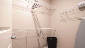 Een hoek van een kamer met een witte muur, een grijze deur en een zwarte prullenbak.