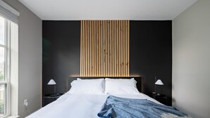 Een moderne slaapkamer met een groot bed, twee nachtkastjes en een houten paneel boven het bed.