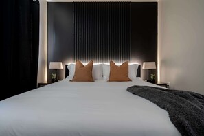 A hotel room with a large bed, two bedside lamps, a dark headboard, and a curtain on the left.