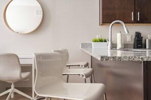 A modern kitchen with a granite countertop, a stainless steel faucet, and a white chair. - Downtown Apt in the Heart of Columbus (Columbus)