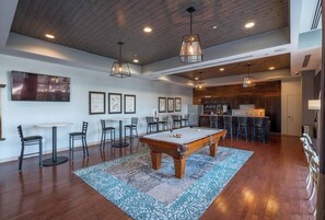 A spacious living area with a pool table, bar seating, and a kitchen area.